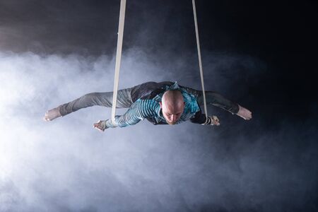 Circus artist on the aerial straps with costume on the black and smoked background.の写真素材
