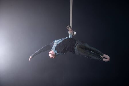Circus artist on the aerial straps with costume on the black and smoked background.