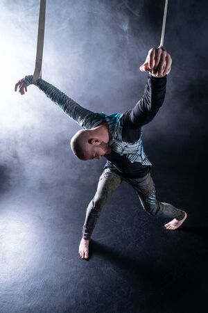Circus artist on the aerial straps with costume on the black and smoked background. Concept of suffering, despair and defeatの写真素材