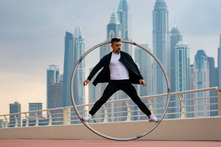 Cyr Wheel artist wearing black and white smart clothes with cityscape background of Dubai during sunsetの写真素材