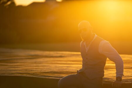Bald Guy with a stylish beard and sunglasses on a blurred city background during sunset. Concept of success and will.の写真素材