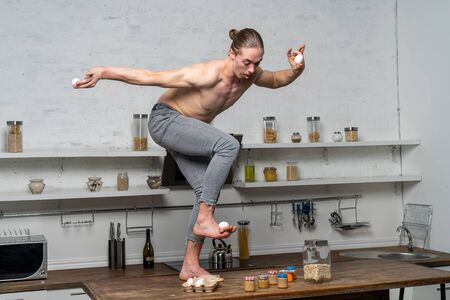 Creative photo of muscular man in the kitchen balancing eggsの写真素材