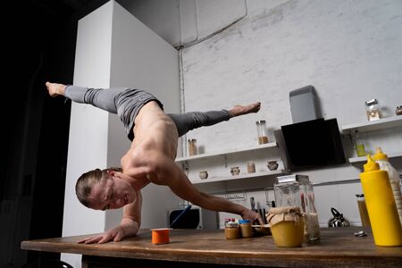 Muscular man stand on the hands in the kitchen and eating yogurt. Concept of healthy lifestyle and organic foodの写真素材