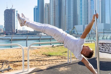Muscular man doing workout on the pole with cityscape of skyscrapers on background in Dubai. Concept of healthy lifestyle and modernの写真素材