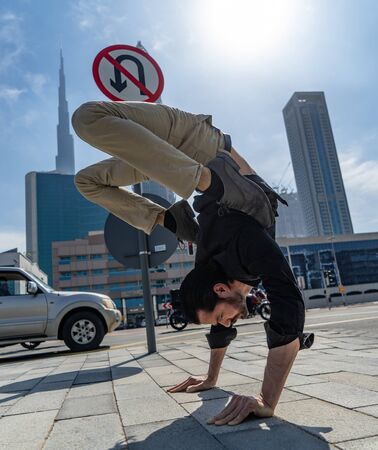 Flexible Acrobat keep balance on the hands with blurred Dubai cityscape and traffic sign U-Turn is prohibited. Concept of modern, business and unlimited possibilityの写真素材