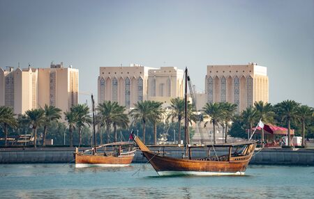 Retro historical boat with blurred panoramic view of modern skyline of Doha and green palms on background.の写真素材