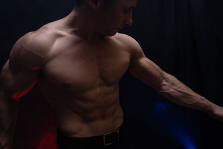 Muscular man showing muscles isolated on the black background with colored smoke. Concept of healthy lifestyleの写真素材