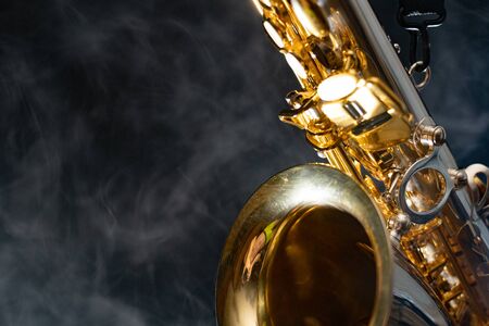 Golden shiny alto saxophone on black background with smoke. copy space
