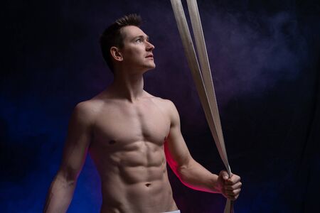 Muscular male circus artist with aerial straps on black and smoked backgroundの写真素材