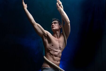 Muscular male circus artist with Cord Lisse on black an smoked backgroundの写真素材