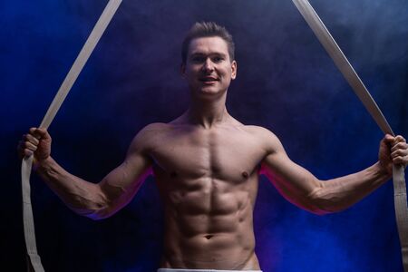Muscular male circus artist with aerial straps on black and smoked backgroundの写真素材