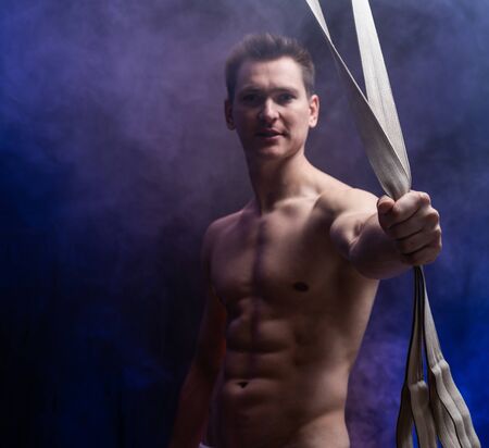 Muscular male circus artist with aerial straps on black and smoked backgroundの写真素材