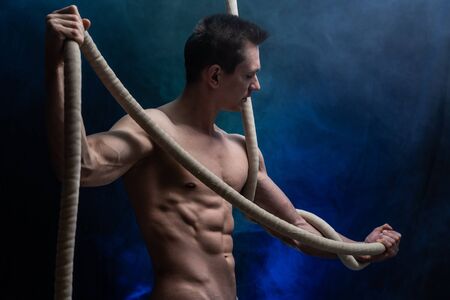 Muscular male circus artist with Cord Lisse on black an smoked backgroundの写真素材