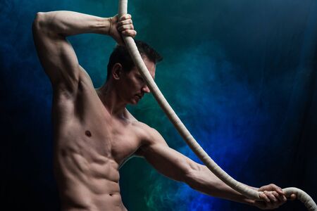 Muscular male circus artist with Cord Lisse on black an smoked backgroundの写真素材