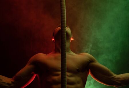 Muscular male circus artist with Cord Lisse on black an smoked background