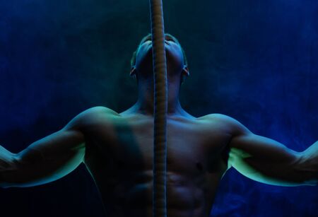 Muscular male circus artist with Cord Lisse on black an smoked background