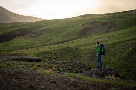 Young hiker man with river and green mountains on background on the Fimmvorduhals hiking trail in Iceland. Concept of freedom movement and freedom.の写真素材