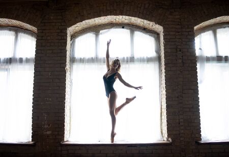 silhouette of a young good shaped ballerina standing on the huge window. Concept of healthy lifestyleの写真素材