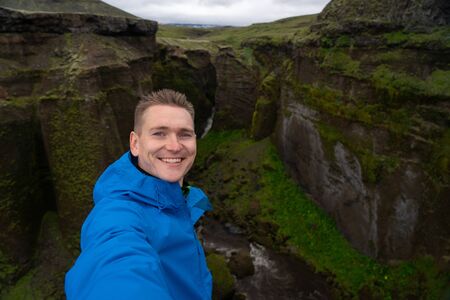 Young smiling man with river and green canyon on background takes a Selfie. Concept of freedom movement and freedomの写真素材
