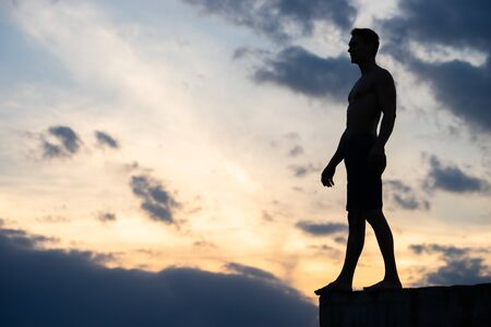 Silhouette of man against background of clouds and sunset. He stands on edge of roof. He is ready to take a step. Concept of Risk and courageの写真素材