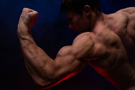 Muscular man showing muscles isolated on the black background with colored smoke. Concept of healthy...