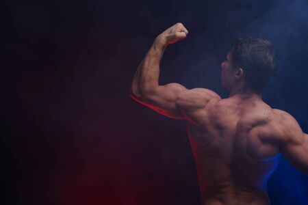 Muscular man showing muscles isolated on the black background with colored smoke. Concept of healthy lifestyleの写真素材