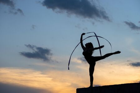 Professional gymnast woman dancer with ribbon on sky backgroundの写真素材
