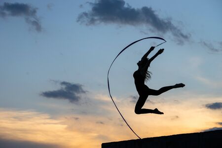Professional gymnast woman dancer with ribbon on sky background