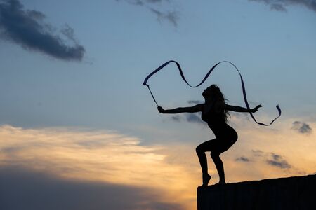 Professional gymnast woman dancer with ribbon on sky backgroundの写真素材