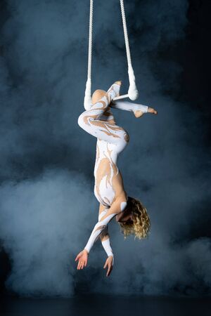 A young girl performs the acrobatic elements in the air trapeze. Studio shooting performances on a black background.の写真素材