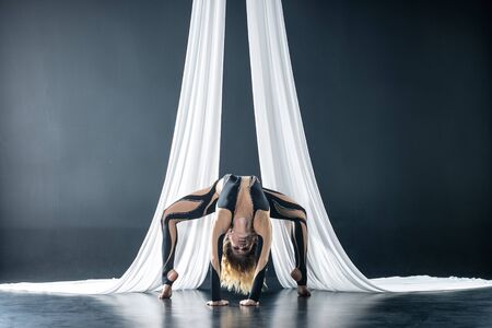 Beautiful flexible woman gymnast with white aerial silks isolated on black backgroundの写真素材