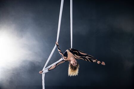 A young girl performs the acrobatic elements in the airrial silk. Studio shooting performances on a black backgroundの写真素材