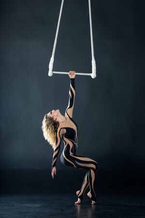A young girl performs the acrobatic elements in the air trapeze. Studio shooting performances on a black background.の写真素材