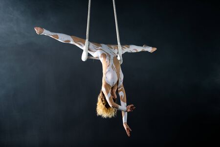 A young girl performs the acrobatic elements in the air trapeze. Studio shooting performances on a black background.の写真素材