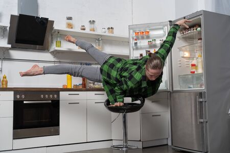 Muscular man balancing on one the hand in the kitchen. Concept of healthy lifestyle and organic foodの写真素材
