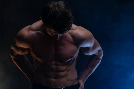 Muscular man showing muscles isolated on the black background with colored smoke. Concept of healthy lifestyle.の写真素材