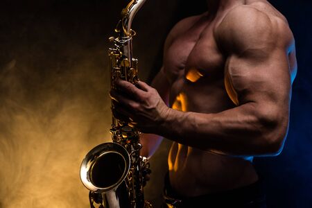 Muscular man with naked torso playing on saxophone with smoked colorful background.の写真素材