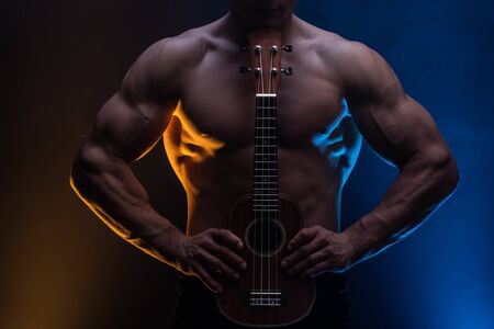 Muscular man with naked torso with ukulele and smoked colorful background.の写真素材