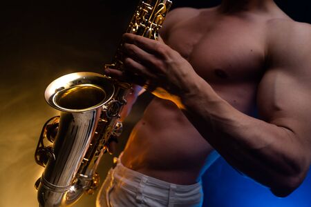 Muscular man with naked torso playing on saxophone with smoked colorful background.の写真素材