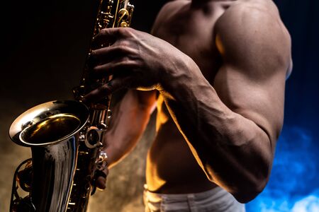 Muscular man with naked torso playing on saxophone with smoked colorful background.の写真素材