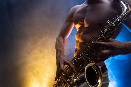 Muscular man naked torso playing on saxophone with smoked colorful backgroundの写真素材