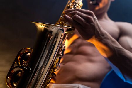 Muscular man naked torso playing on saxophone with smoked colorful backgroundの写真素材