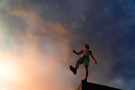 Muscular man stepping from the edge during dramatic sunset. Concept of choice and courageの写真素材
