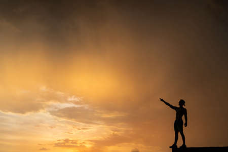 Man standing on the edge rising hands on dramatic orange sunset background. Concept of desire and achievementの写真素材