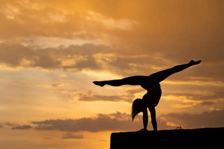 Flexible girl doing exercise on sky background during dramatic sunsetの写真素材