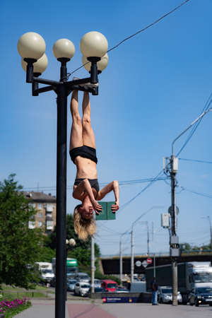 Girl hanging by feet upside down in the street on the Street light and reading book. Concept of...