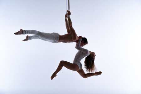 Aerial straps duo wearing white costume on white background doing performance