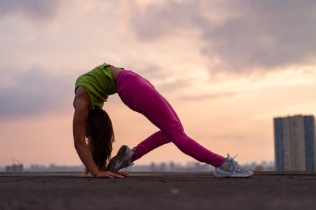 Flexible woman doing poses outdoor on the dramatic sunset background. Concept of activity, healthy lifestyle and wellnessの写真素材