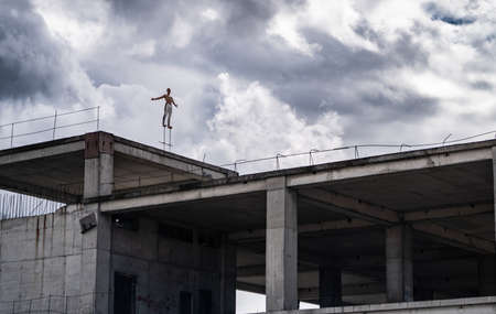 Man standing on the edge of rooftop unfinished building with dramatic clouds on background. Concept of Courage, inspiration and freedomの写真素材