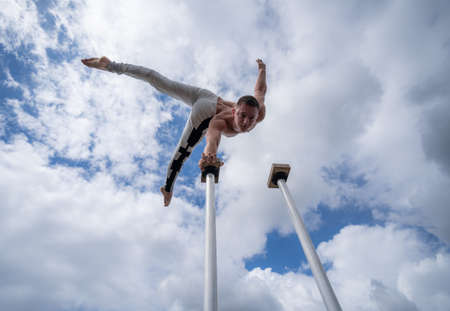 Flexible male circus Artist keep balance by one hand against amazing cloudscape. Individuality, outstanding and originality.の写真素材